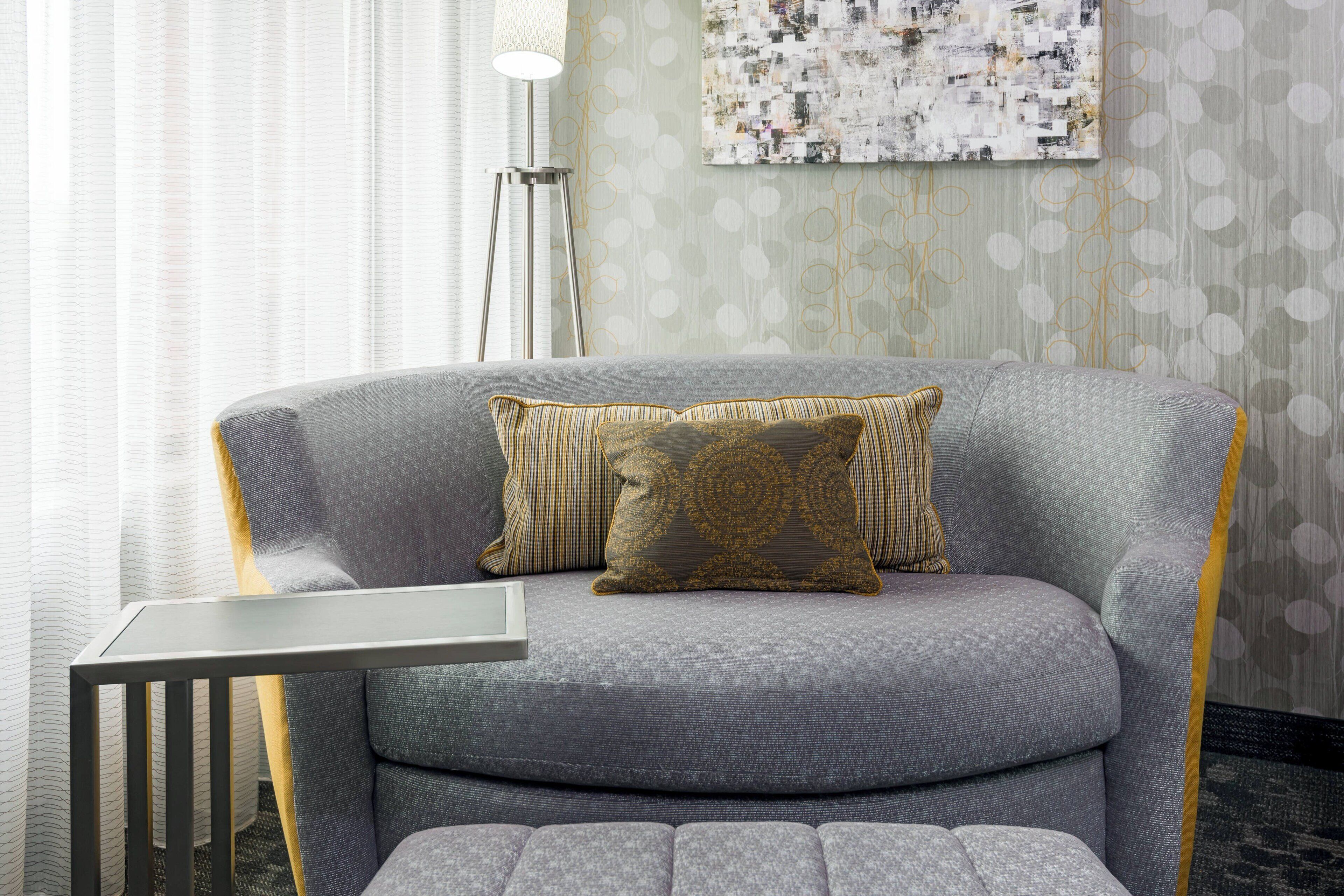A modern living room with a grey sofa, a patterned throw pillow, a small side table, and a floor lamp.