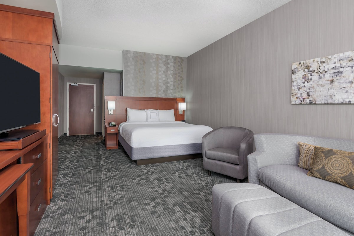 A hotel room with a bed, a sofa, a TV, a desk, and a wall art piece.