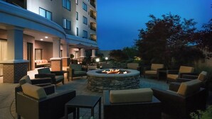 Un área de patio al aire libre con un hogar de piedra rodeado de muebles de mimbre y cojines.