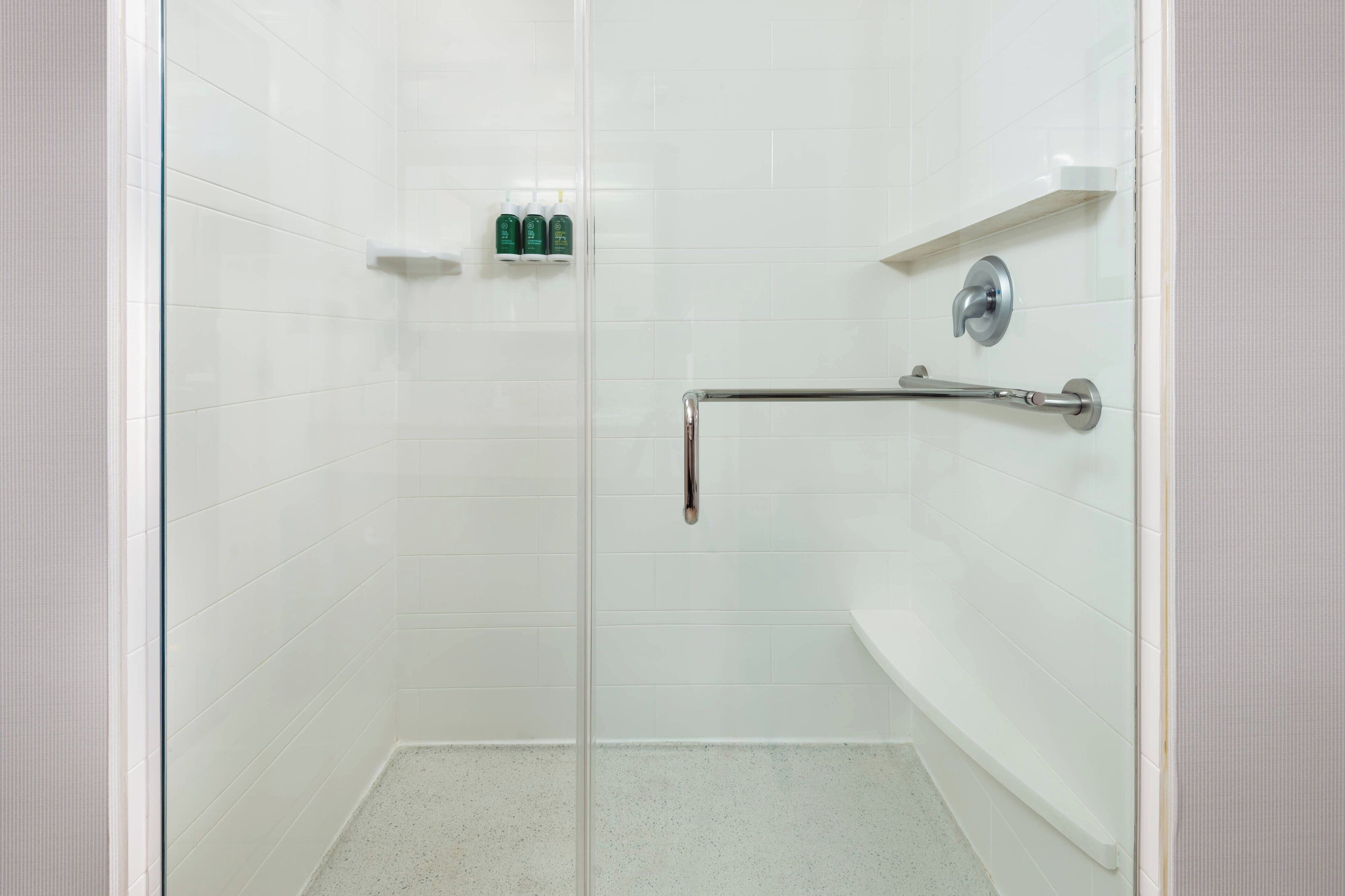 A walk-in shower with white tiles, a glass door, and a grab bar.