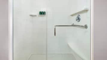 A walk-in shower with white tiles, a glass door, and a grab bar.