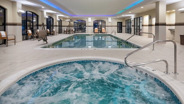 Un área de piscina de hotel con un jacuzzi, sillas de descanso y un espacio de estar con mesas.