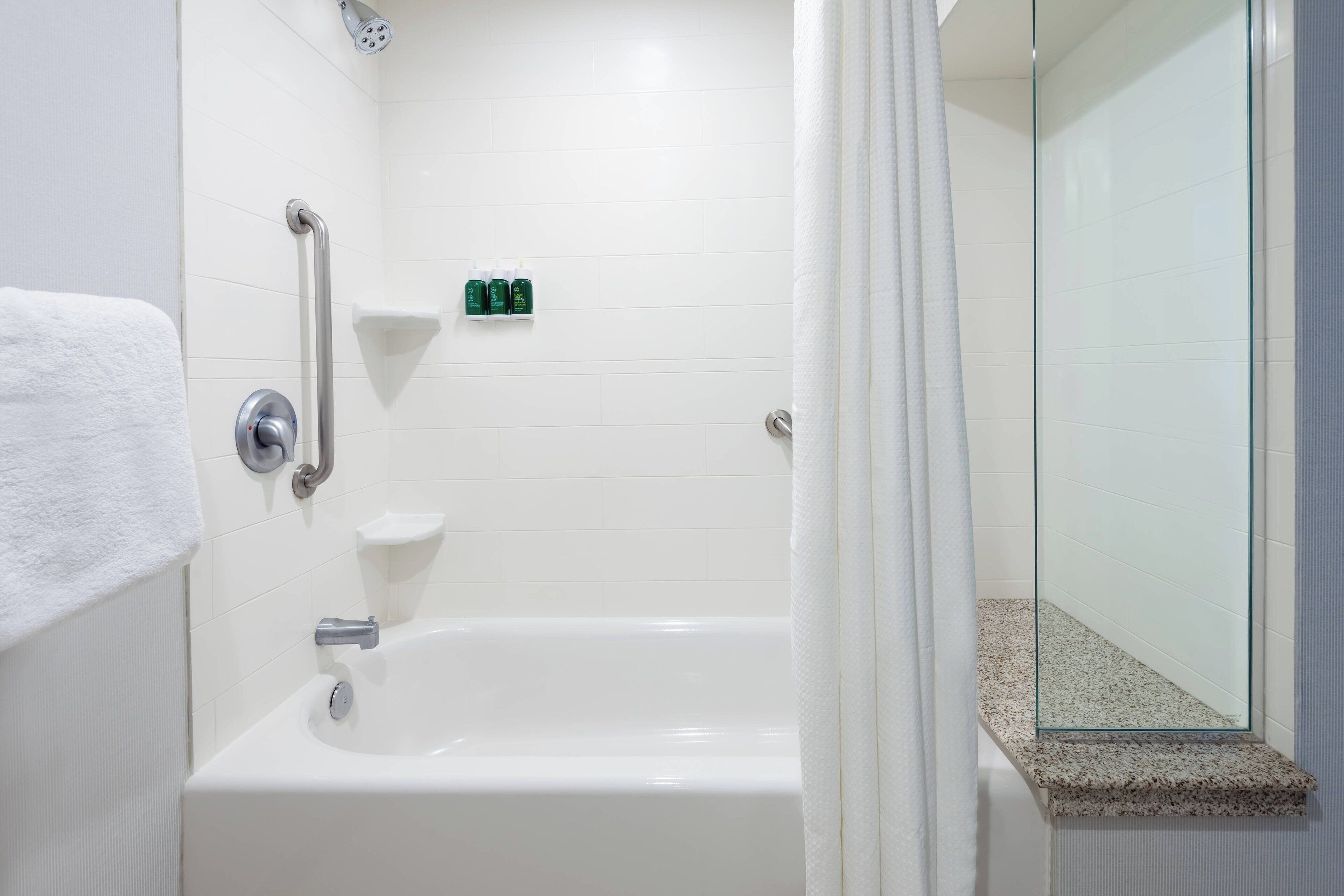 A modern bathroom with a white bathtub, a glass shower enclosure, and a handrail.