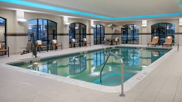 A pool area with lounge chairs and tables, surrounded by glass walls and a tiled floor.