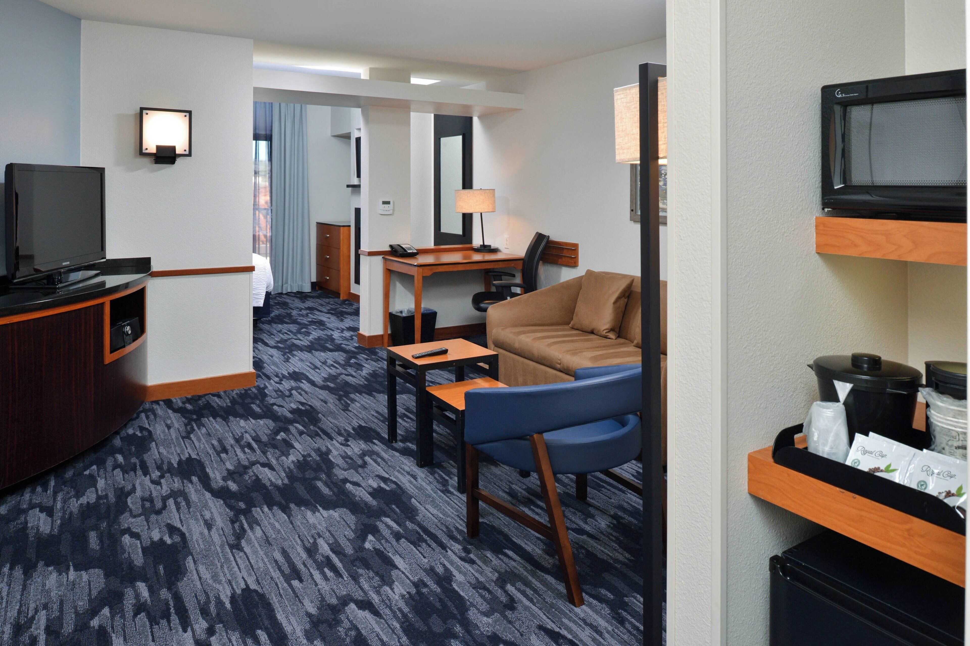 A hotel room with a television, a desk with a lamp, a sofa, and a microwave.