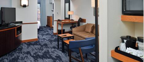 A hotel room with a television, a desk with a lamp, a sofa, and a microwave.
