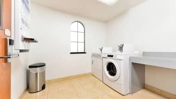 Una sala de lavandería con lavadora, secadora y un cubo de basura.