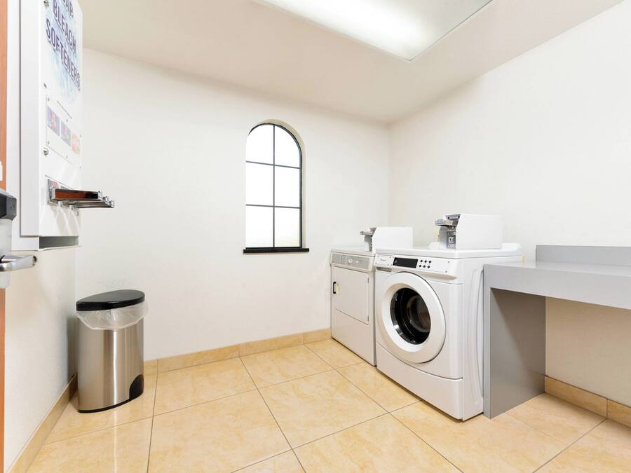 Una sala de lavandería con lavadora, secadora y un cubo de basura.
