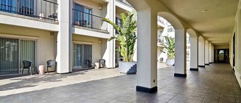 A spacious indoor corridor with tiled flooring, large potted plants, and multiple balconies with railings.