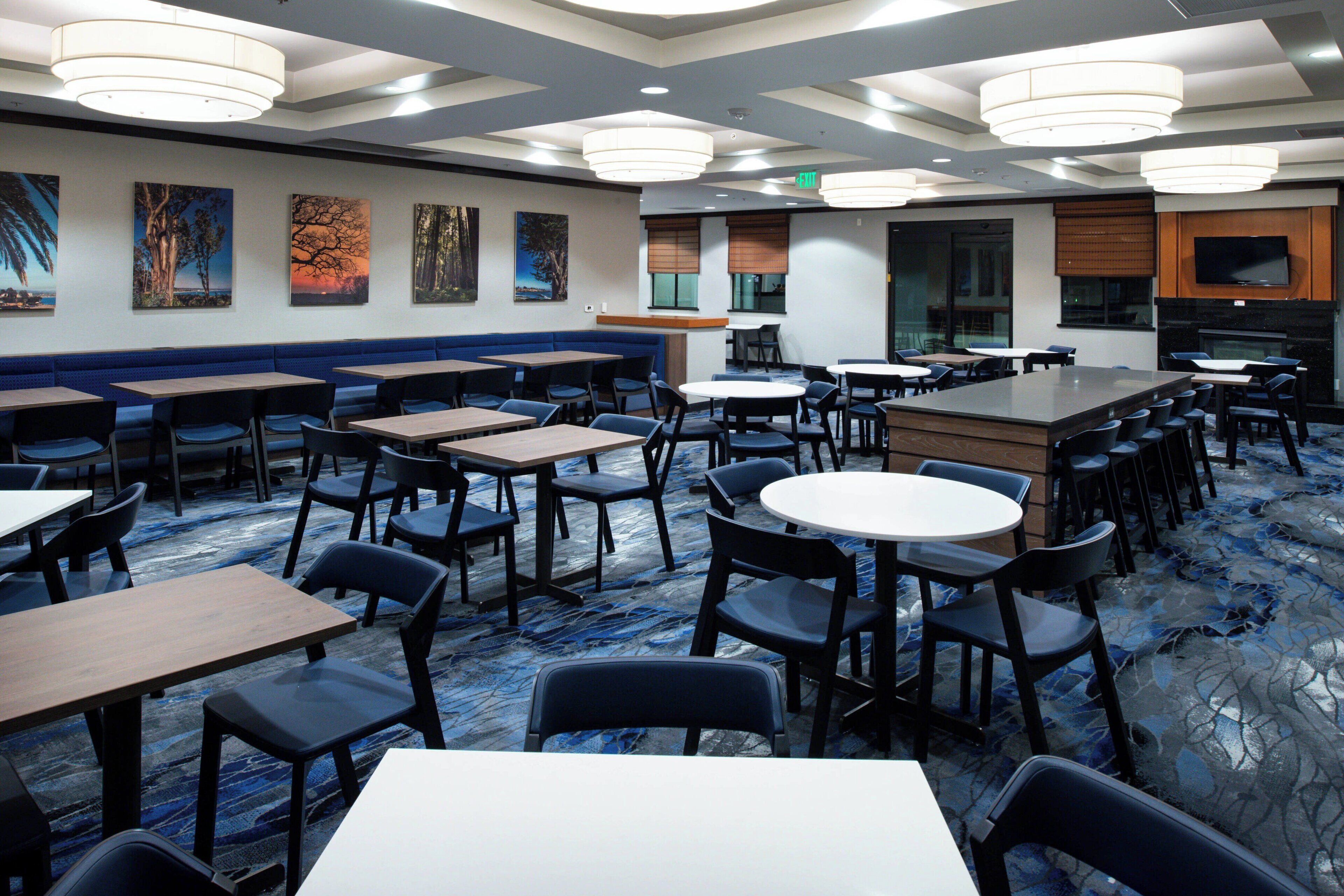 A hotel dining area with multiple tables and chairs, a blue carpet, and wall art.
