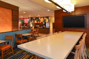 Un restaurant doté d’une longue table en bois, de plusieurs chaises, d’un coin bar et d’un écran de télévision fixé au mur.