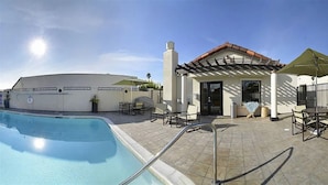 Uma área de piscina com céu claro, um edifício com telhado telhado e mobiliário de exterior.