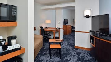 A hotel room with a kitchenette, a TV, a desk with a chair, a lamp, and a bed.
