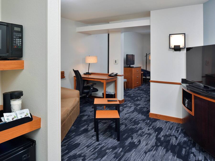 A hotel room with a kitchenette, a TV, a desk with a chair, a lamp, and a bed.