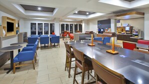 A modern dining area with blue and red chairs, a long table, and a coffee station. - Holiday Inn Express Hotel & Suites Niles by IHG (Niles)