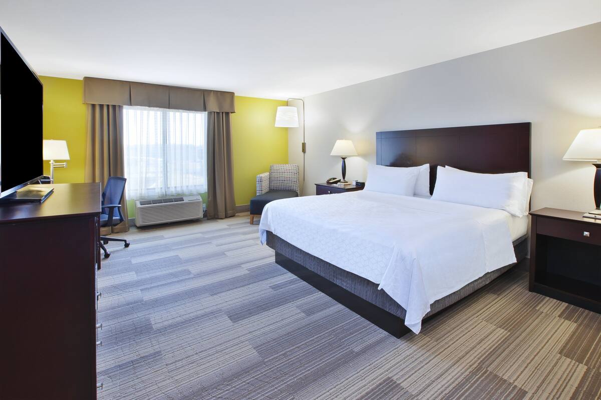 A hotel room with a large bed, a desk with a chair, a TV, and a window with curtains.