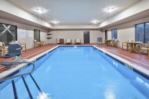 A swimming pool with a diving board, lounge chairs, and a table with chairs.
