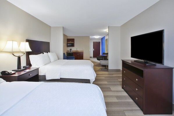 Een hotelkamer met twee bedden, een televisie, een bureau met lamp en een kitchenette op de achtergrond.