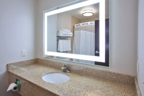 Een badkamer met een granieten aanrecht, een wastafel, een spiegel en een handdoekrek met opgevouwen handdoeken.