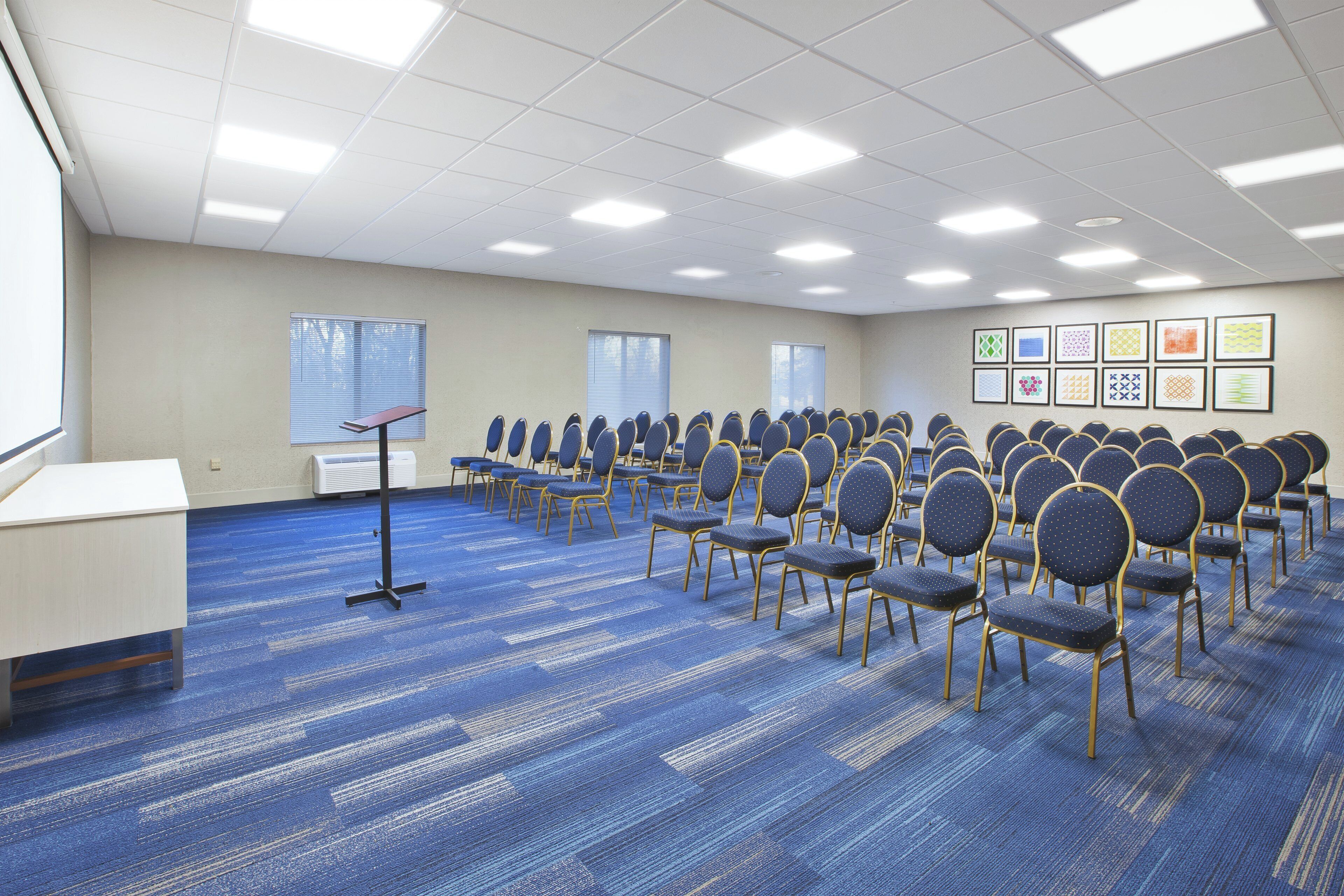 A conference room with rows of chairs, a podium, and framed artwork on the wall.