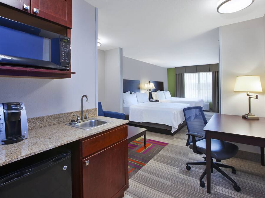 A hotel room with a kitchenette, a bed, a desk, and a chair.