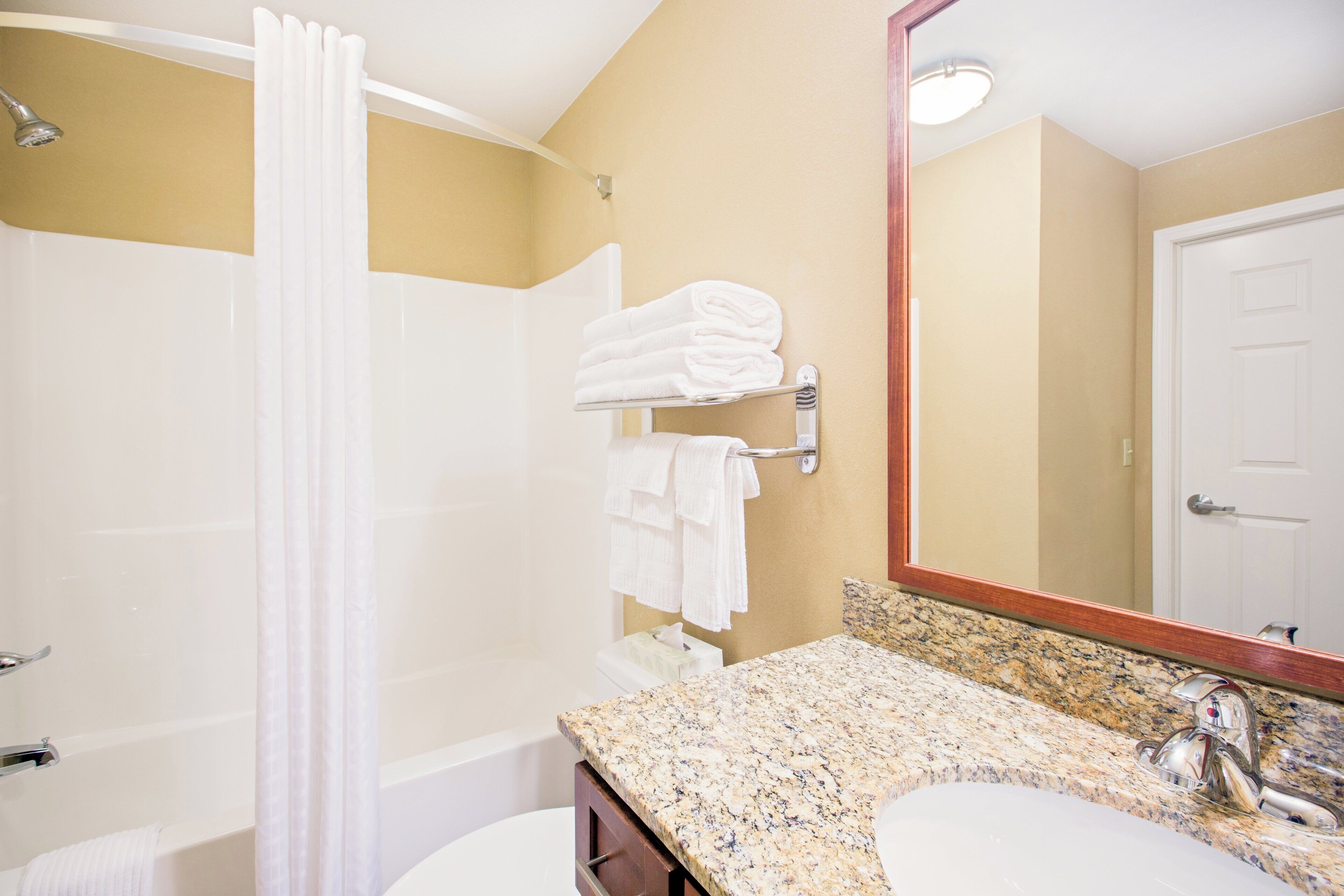 A bathroom with a shower, a sink, a mirror, and towels.