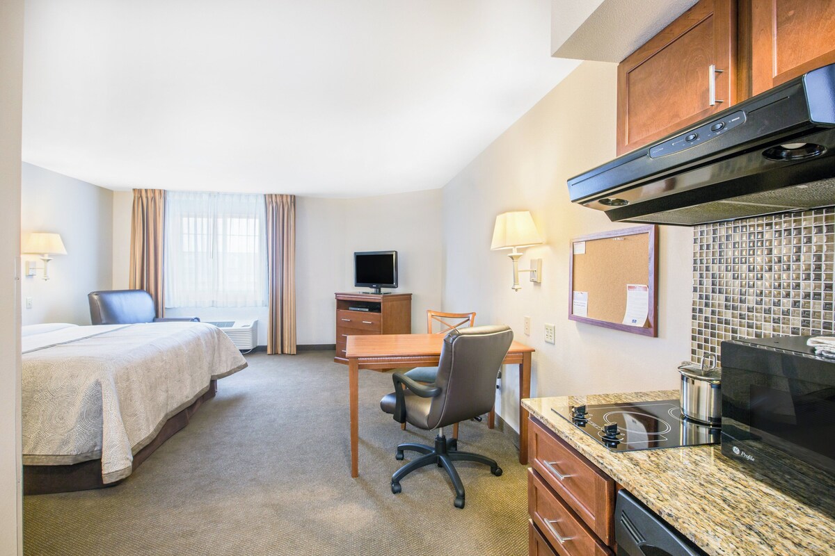Habitación de hotel con cama, escritorio, silla, kitchenette y televisor.