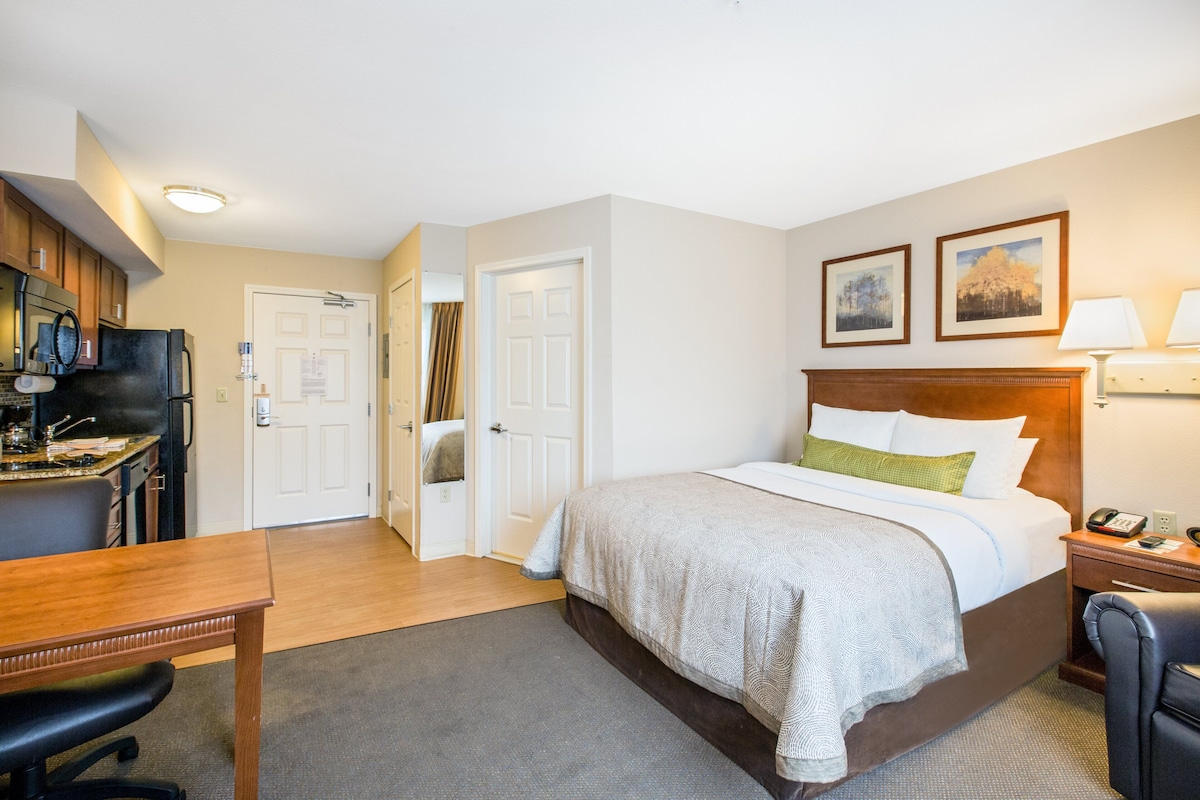 Een hotelkamer met een bed, bureau en kitchenette.