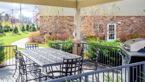 An outdoor patio with a table and chairs, a grill, and a view of a brick building and garden. - Candlewood Suites Pittsburgh Cranberry by IHG (Cranberry Township)
