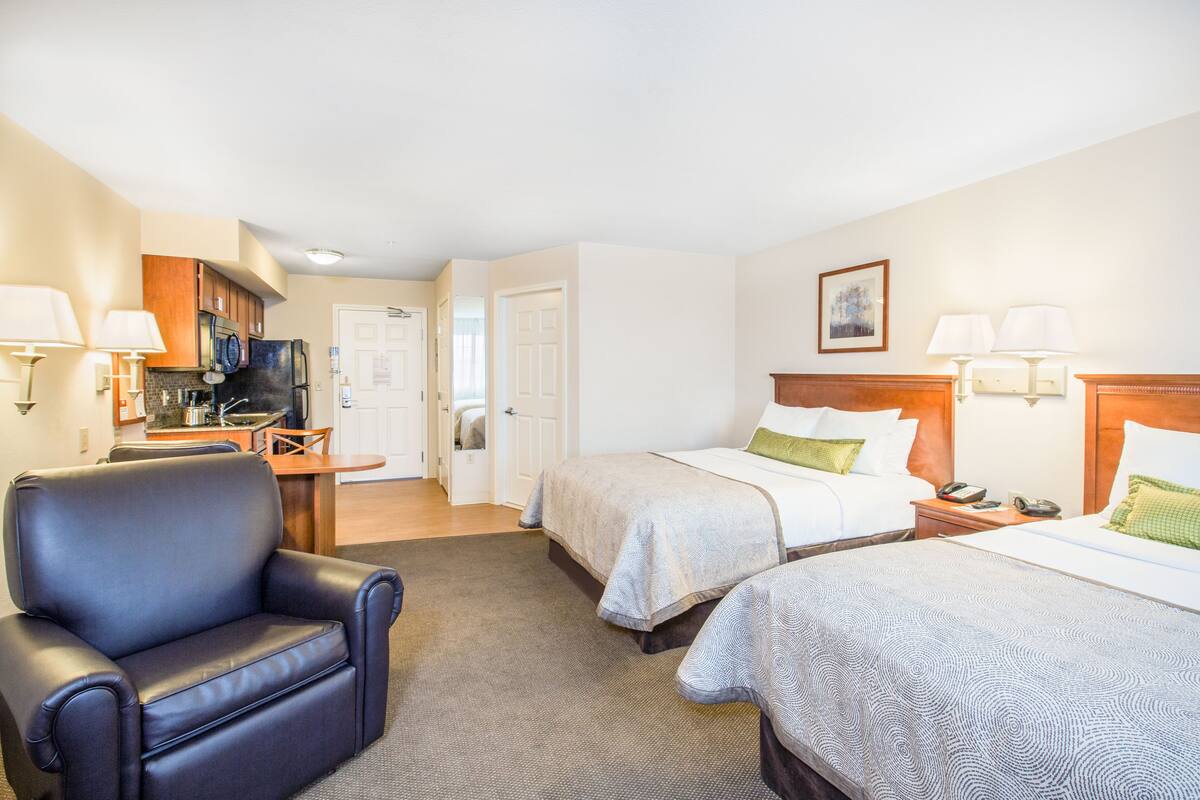 Une chambre d’hôtel avec deux lits, une chaise, un bureau et une kitchenette.