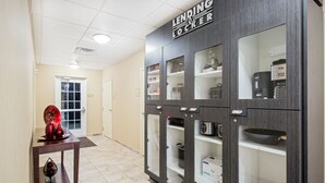 Een gang met een 'Lending Locker' kast, waarin diverse items zitten zoals een koffiezetapparaat, een waterkoker en een doosje met de tekst 'DRINK'.