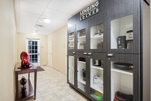 Un pasillo con un armario 'Lending Locker' que contiene varios artículos, como una cafetera, un hervidor y una caja etiquetada 'DRINK'.