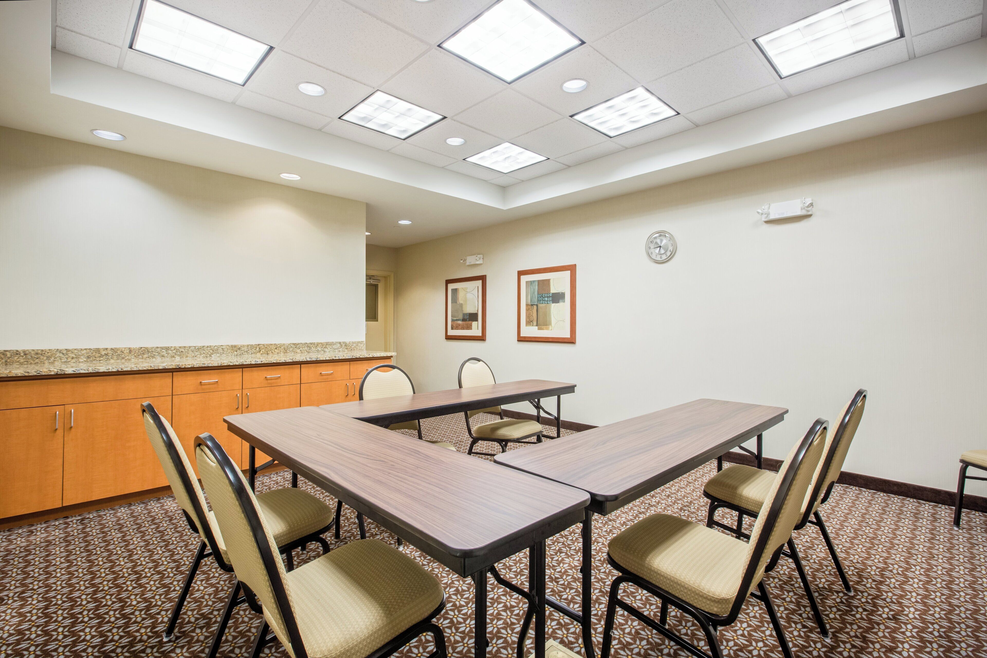 Une salle de conférence avec une table rectangulaire, six chaises, une horloge et une fenêtre.