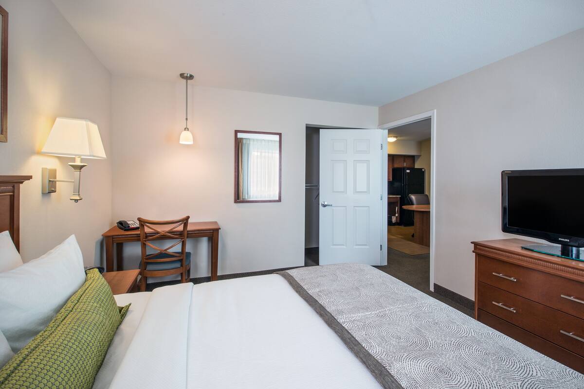 Une chambre d’hôtel équipée d’un lit, d’un bureau, d’une chaise, d’une télévision et d’une porte donnant sur un coin cuisine.