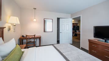 A hotel room with a bed, a desk, a chair, a television, and a door leading to a kitchen area.