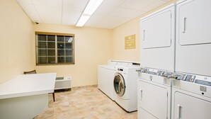 Een wasserette met een wasmachine, droger en een tafel met stoelen.