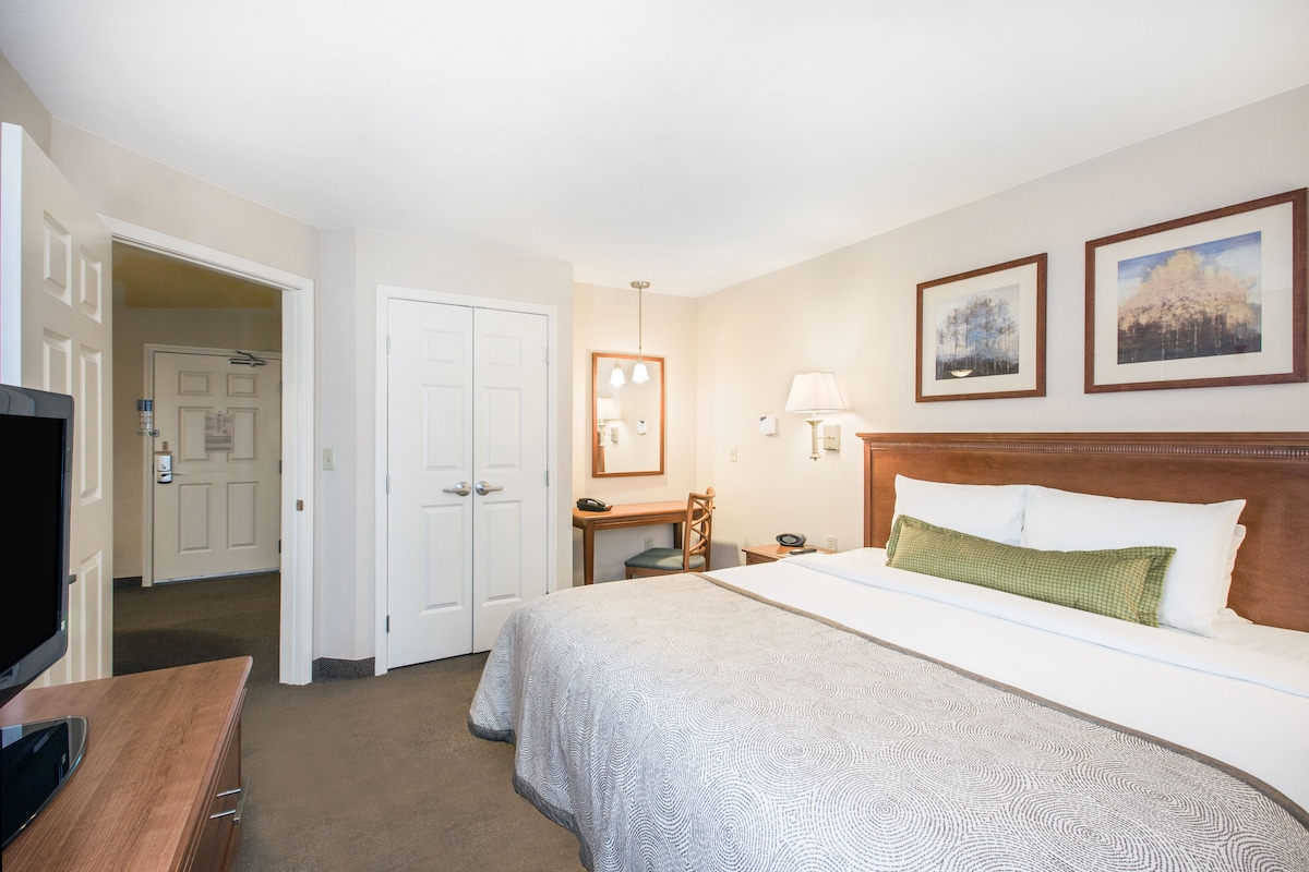 Een hotelkamer met een bed, een bureau, een televisie en een deur naar een andere kamer.
