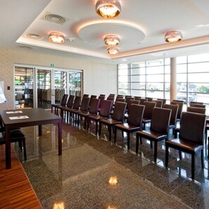 A conference room with a long table and chairs, large windows, and ceiling lights.
