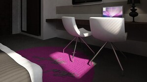 Ein modernes Schlafzimmer mit einem Bett, einem Schreibtisch mit Computer, zwei Stühlen, einem Fernseher und einer Lampe.