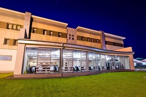 A modern building with a curved glass facade, multiple floors, and a well-maintained lawn. - Hotel Symfonia (Osjakow)