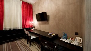 Ein Hotelzimmer mit Schreibtisch, Stuhl, Fernseher und einem Fenster mit roten Vorhängen.