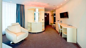 Ein Hotelzimmer mit rundem Schreibtisch, einem runden Sessel, einem an der Wand befestigten Fernseher und einem kleinen Tisch mit Stuhl.
