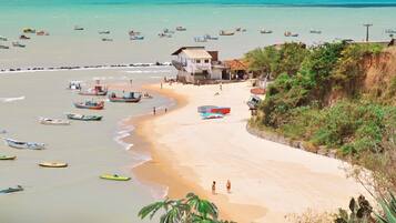 Uma praia com barcos, um edifício com placa e um penhasco com vegetação.