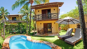 Una casa de dos pisos con piscina, mobiliario de exterior y jardín.