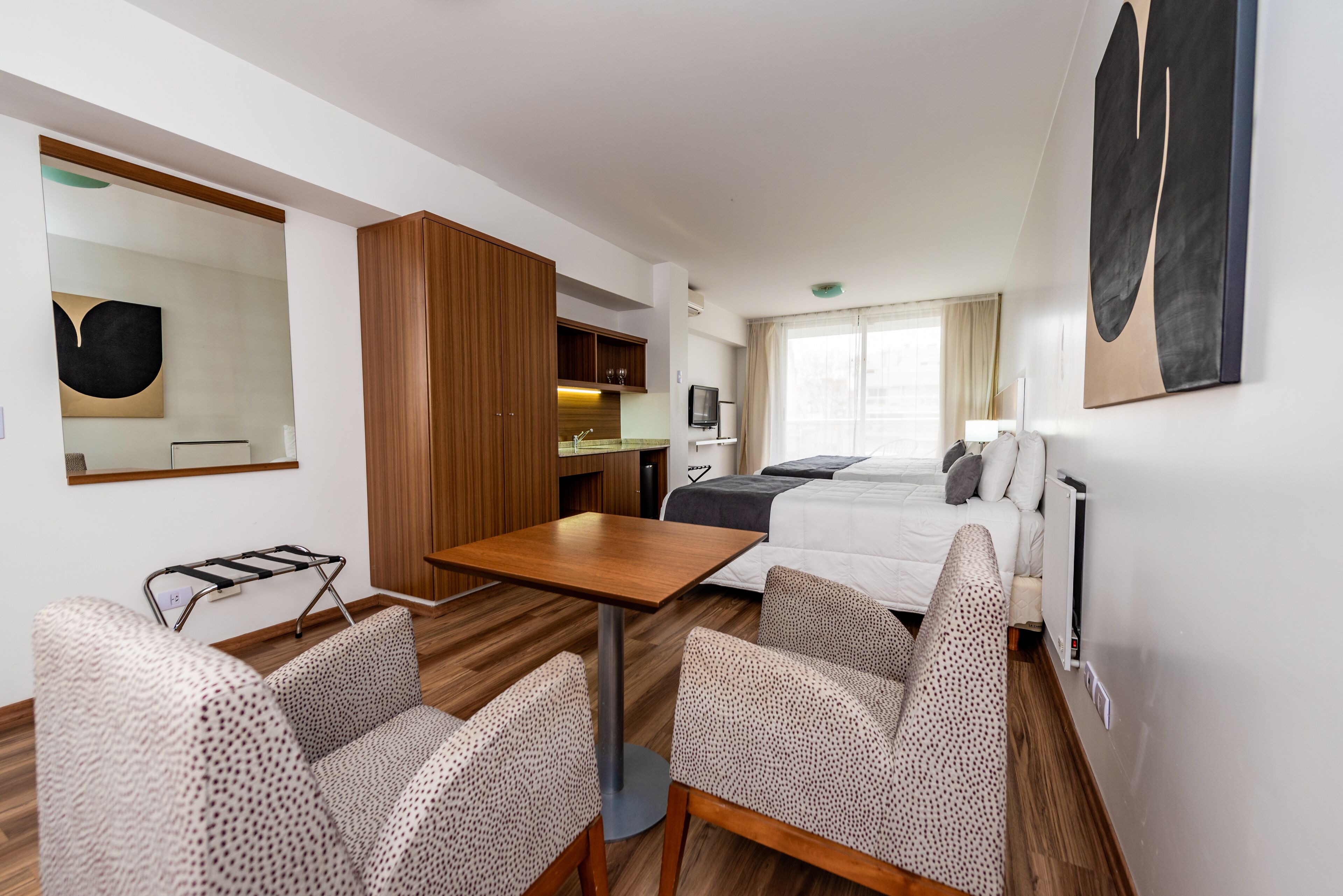 Ett hotellrum med en säng, ett skrivbord, en stol, ett litet pentry och ett stort fönster.
