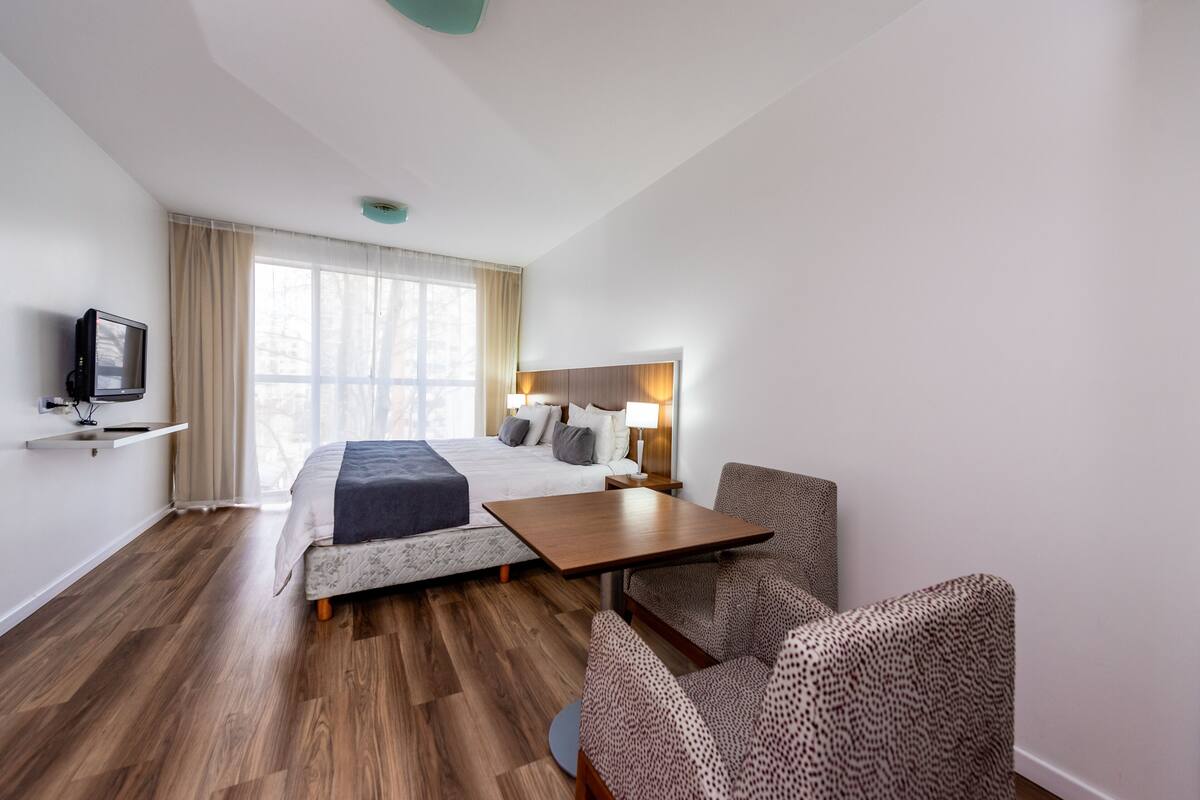 A hotel room with a bed, a desk, a chair, a TV, and a window with curtains.