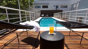 A poolside area with lounge chairs, a table with a drink, and a view of the pool. - Hotel Bys Palermo (Buenos Aires)