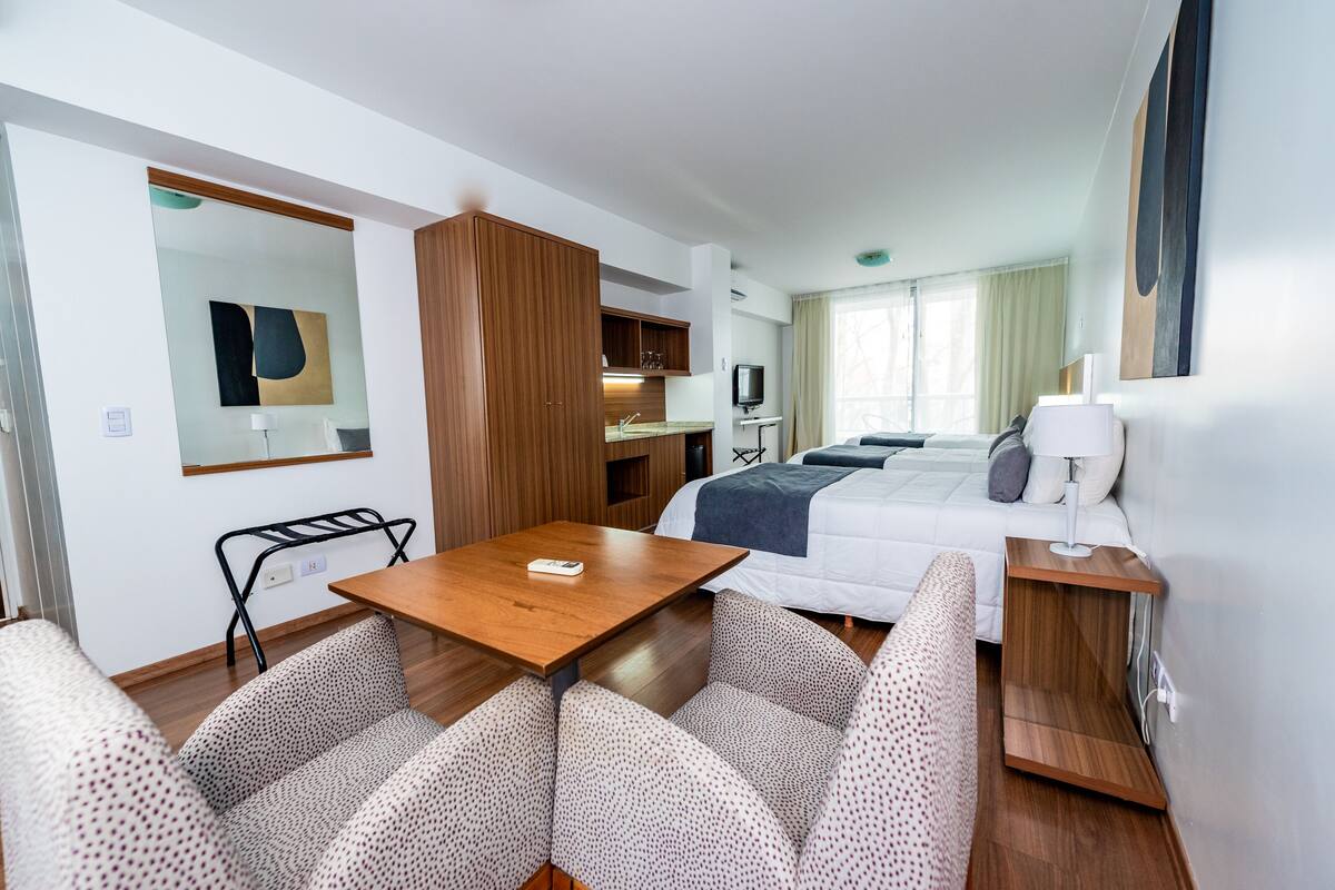 A compact hotel room with a bed, a small desk, a chair, a sofa, and a TV.