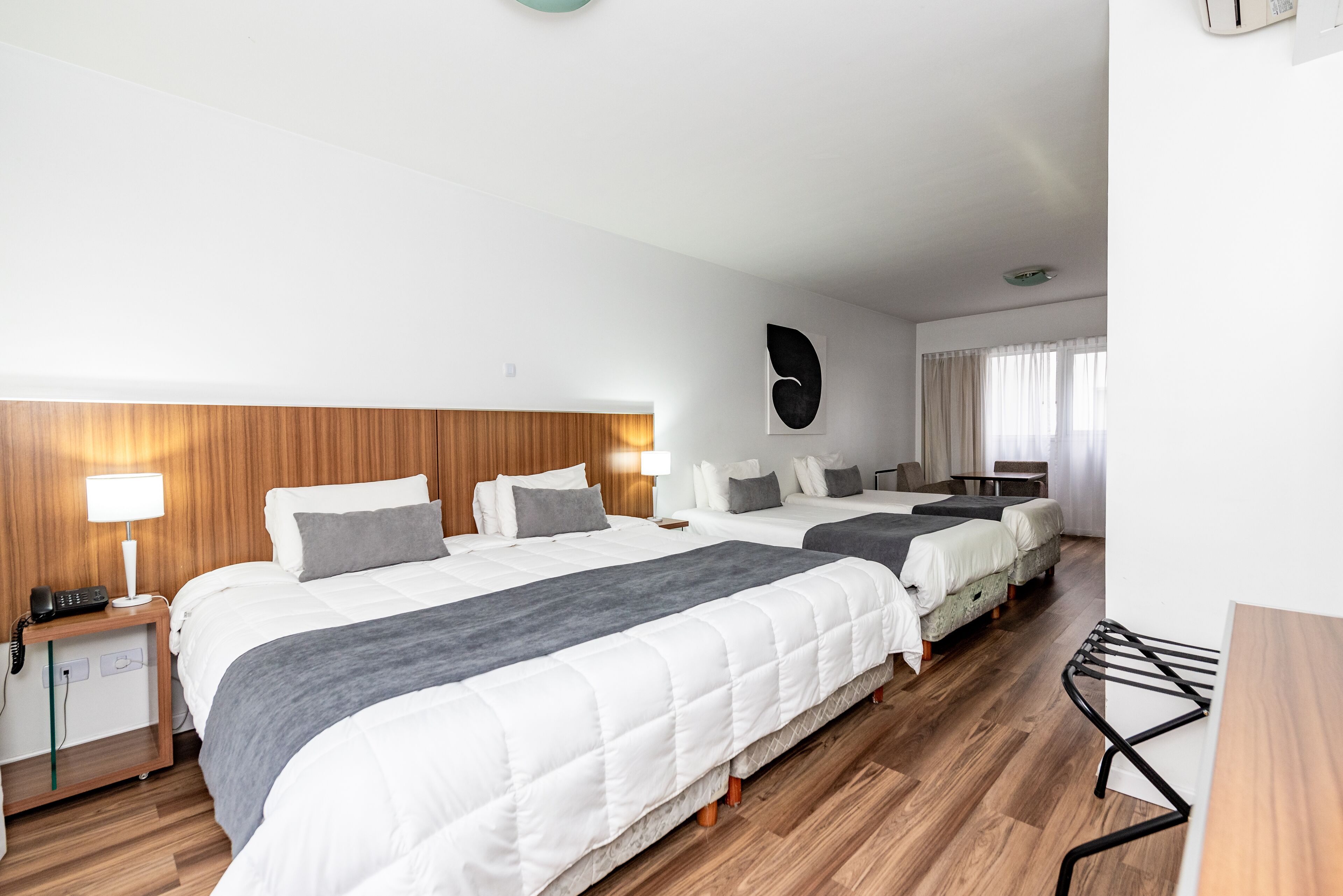 Ett hotellrum med två sängar, sänggavlar i trä, ett nattduksbord med en lampa och ett stort fönster med gardiner.