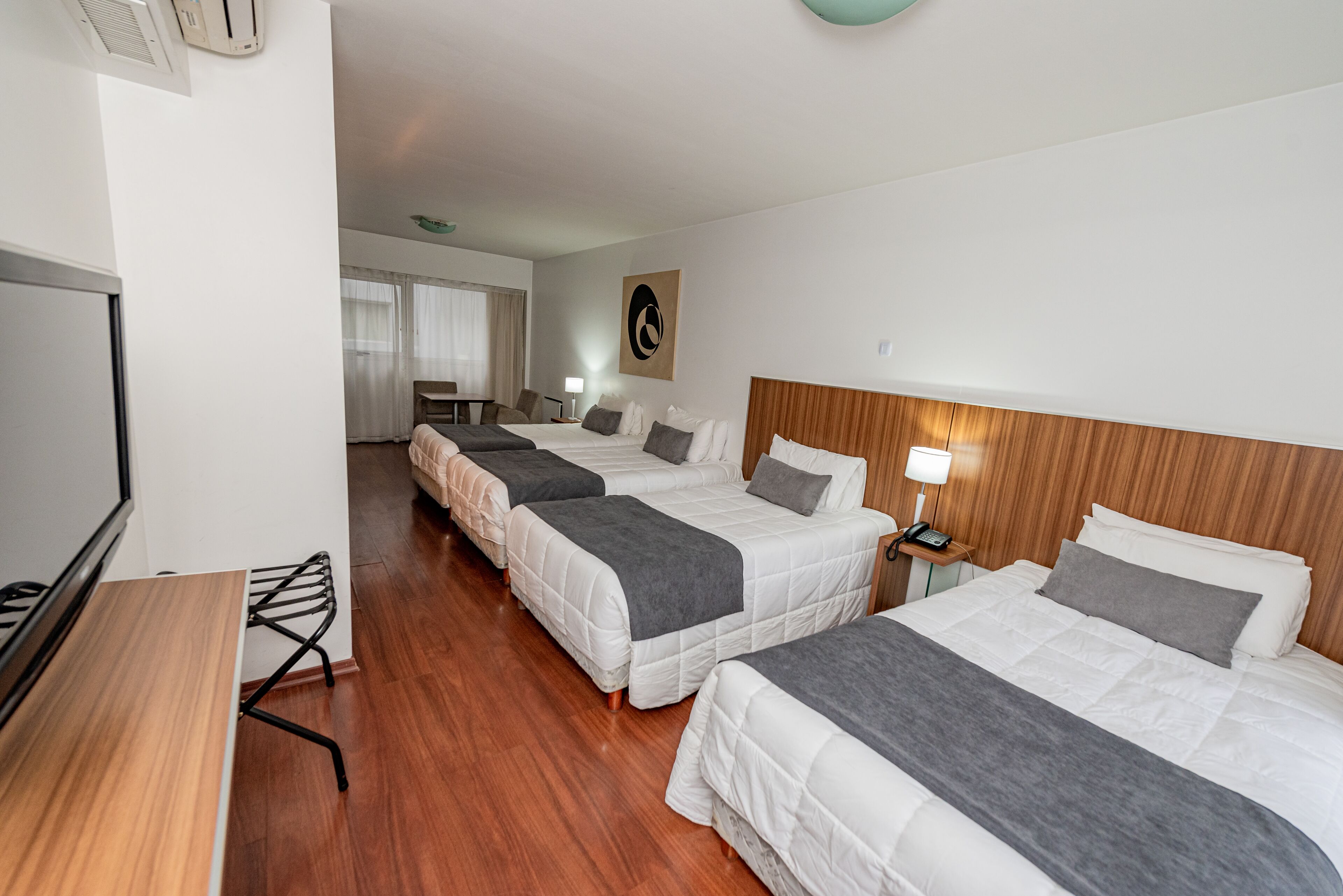A hotel room with three beds, a desk, and a television.